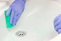 Female hand in a blue glove wipes the sink with a green foam sponge in the bathroom Royalty Free Stock Photo