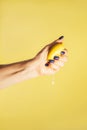 Female hand with blue nails hold fresh lemon isolated on yellow. Squeeze out juice. Finger crush. Vertical, copy space Royalty Free Stock Photo