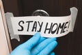 Female hand in blue rubber gloves holding door lock quarantine message glued to metal brown door of house. Stay home. Coronavirus