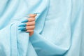 Female hand with blue stiletto nail design. Long nail polish manicure. Woman hand on blue fabric background