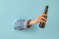 Female hand with bottle of beer breaks through blue paper background. Royalty Free Stock Photo
