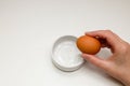 Female hand breaking a raw egg into a white cup standing on a white background Royalty Free Stock Photo
