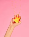 Female hand with bright manicure squeezes half of orange. Pop art food photography. Drops of juice fly up