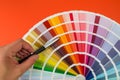 Female hand chooses color in palette swatches. Rainbow colors catalog isolated on orange Royalty Free Stock Photo