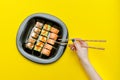 Female hand with chopsticks and plate with various rolls. Yellow