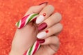 Female hand with Christmas nail design. Glitter red and glossy white nail polish manicure. Woman hand hold Christmas candy on Royalty Free Stock Photo