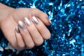 Female hand with Christmas nail design. Silver nail polish manicure. Female hand on blue New Year tinsel background