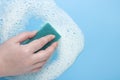 Female hand with a cleaning sponge in white foam, mousse on a blue background. The concept of foaming products, detergents or Royalty Free Stock Photo