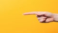 Female hand close-up, long index finger pointing at something. Gesture of direction. Yellow background. Copy space Royalty Free Stock Photo