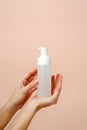 Female hand with cosmetic product in bottle on neutral beige trendy background, concept of helathcare, hygiene, dispenser with