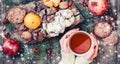 Female hand a cup of tea. Christmas Cookies Chocolate, tea, pomegranate, Tangerines, Nuts, cocoa beans on wooden snowy background