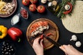 Female hand cut chilli, mushrooms and tomatoes on wooden board on kitchen table, around lie ingredients for pizza Royalty Free Stock Photo