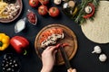 Female hand cut chilli, mushrooms and tomatoes on wooden board on kitchen table, around lie ingredients for pizza Royalty Free Stock Photo