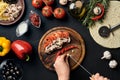 Female hand cut garlic, chilli, mushrooms and tomatoes on wooden board on kitchen table, around lie ingredients for Royalty Free Stock Photo