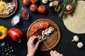 Female hand cut mushrooms and tomatoes on wooden board on kitchen table, around lie ingredients for pizza: vegetables Royalty Free Stock Photo