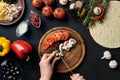 Female hand cut mushrooms and tomatoes on wooden board on kitchen table, around lie ingredients for pizza: vegetables Royalty Free Stock Photo