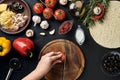 Female hand cut tomatoes on wooden board on kitchen table, around lie ingredients for pizza: vegetables, cheese and Royalty Free Stock Photo