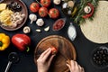 Female hand cut tomatoes on wooden board on kitchen table, around lie ingredients for pizza: vegetables, cheese and Royalty Free Stock Photo