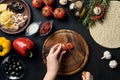 Female hand cut tomatoes on wooden board on kitchen table, around lie ingredients for pizza: vegetables, cheese and Royalty Free Stock Photo