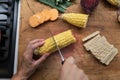Female hand cutting fresh corn cob in half on a wooden cutting board Royalty Free Stock Photo