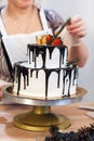 Female hand decorates a white cream cake with fruit, close-up