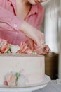 Female hand decorating pink flower wedding birthday cake on stand. Close up pastry chef decoration delicious dessert dish Royalty Free Stock Photo