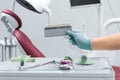 Female hand of dentist in blue gloves holding shade guide, blurred background of clinic with dental unit, dentistry and teeth care Royalty Free Stock Photo