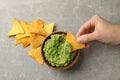 Female hand dips chips slice in guacamole, top view