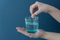 Female hand drops an effervescent tablet into a transparent glass with water on a blue background.