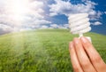 Female Hand with Energy Saving Light Bulb Over Fie Royalty Free Stock Photo