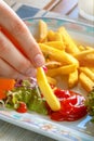 Female hand fingers holding and dipping fried French fries in tomato ketchup on a plate, beautiful vegetarian Breakfast