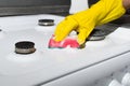 Female hand in glove cleaning the surface of gas stove with washing sponge and chemical foam. Home cleaning concept, kitchen