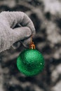 Female hand in gloves hold Green shiny trendy Christmas ball on snowy branch firs in winter forest. Winter holiday Royalty Free Stock Photo