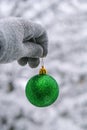 Female hand in gloves hold Green shiny trendy Christmas ball on snowy branch firs in winter forest. Winter holiday Royalty Free Stock Photo