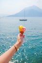 Female hand with golden bracelet watch holding a yellow and pink ice-cream coan with a boat in the sea and mountain in Royalty Free Stock Photo