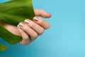 Female hand with golden nail design. Golden nail polish manicure. Female hand with green leaf on blue background