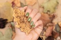 Female hand with green autumn nail design. Woman hand hold dry leaf. Autumn nail polish manicure with golden glitter Royalty Free Stock Photo