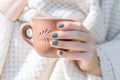 Female hand with green nail design. Glitter green nail polish manicure. Woman hand hold brown ceramic cup