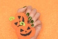 Female hand with green nail design. Glitter green nail polish manicure. Female hold orange paper halloween pumpkins on glitter
