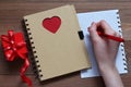 The female hand with the handle does notes on the sheet of paper of a notebook with red heart on a wooden table Royalty Free Stock Photo