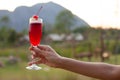 A female hand having a high glass of red cocktail decorated with red cherry with mountain view. Royalty Free Stock Photo