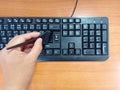 Female hand hold the black brush for cleaning the black keyboard with wooden background. The enter button broken from keyboard