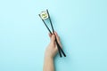 Female hand hold chopsticks with maki on blue background Royalty Free Stock Photo