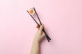 Female hand hold chopsticks with maki on pink background Royalty Free Stock Photo