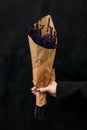 Female hand hold delicate fragnant lavender flowers bouquet wrapped in paper on dark background