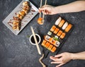 Female hand hold sushi roll with chopsticks on black stone background Royalty Free Stock Photo