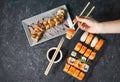 Female hand hold sushi roll with chopsticks on black stone background Royalty Free Stock Photo