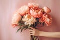 Female hand hold white peonies flowers bouquet on white wall.