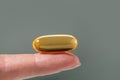 Female hand holding a big yellow capsule of nutritional supplement. Food supplement, vitamin D, omega, vitamin C.