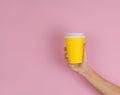 hand holding blank yellow cup with takeaway drink on a pink background ,copy space